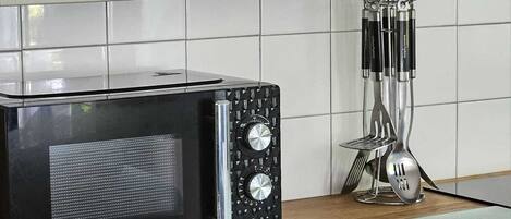 A kitchen with a black microwave, a wooden countertop, and a metal utensil holder.