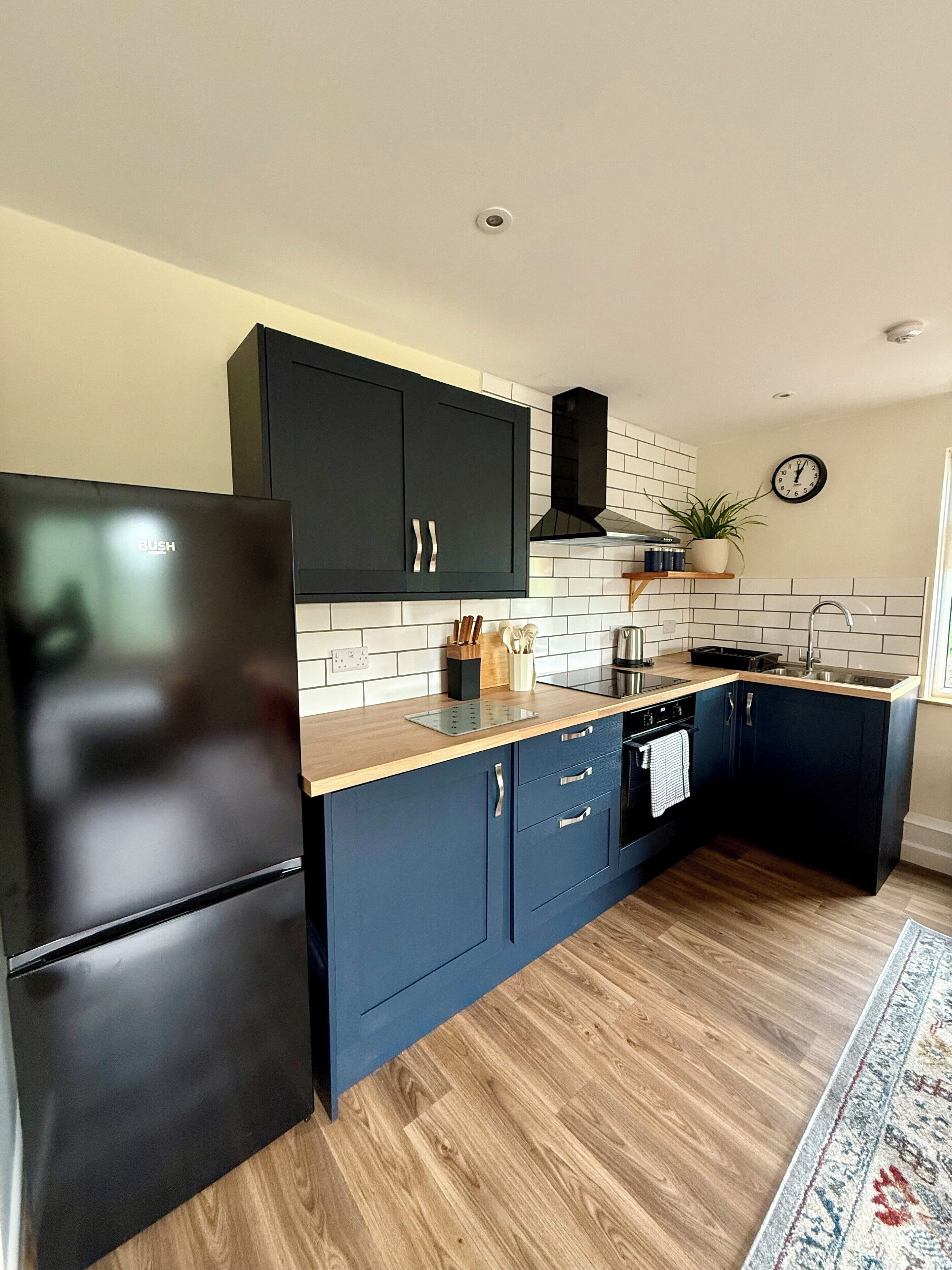 A modern kitchen with dark blue cabinets, a black refrigerator, and a wooden countertop.