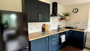 A modern kitchen with dark blue cabinets, a black refrigerator, and a wooden countertop.