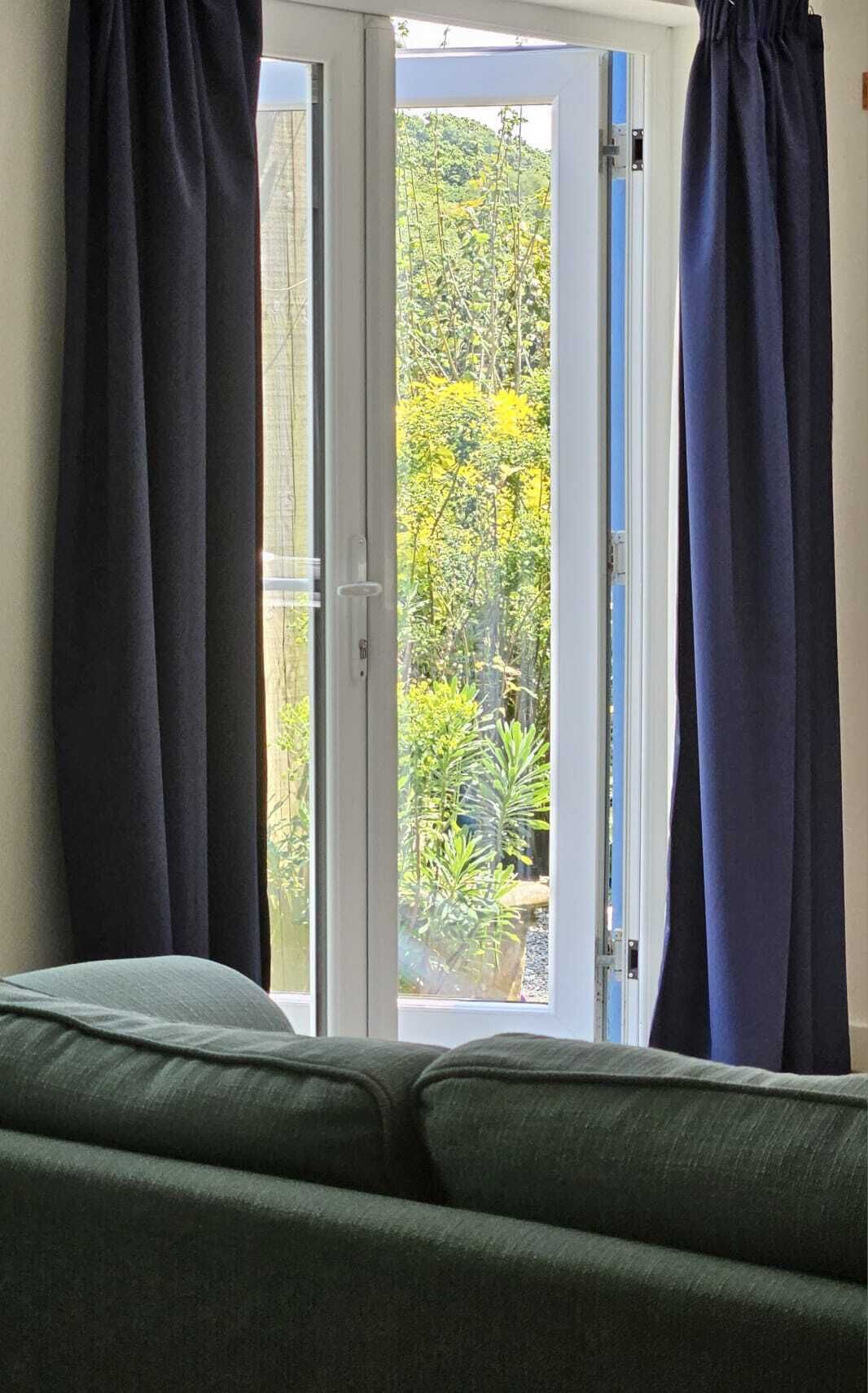 A room with a green sofa, a sliding glass door, and dark curtains.
