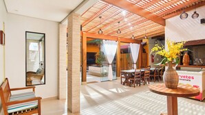 Un interior moderno con techo de madera, un comedor con mesas y sillas, y una recepción con un jarrón de flores.