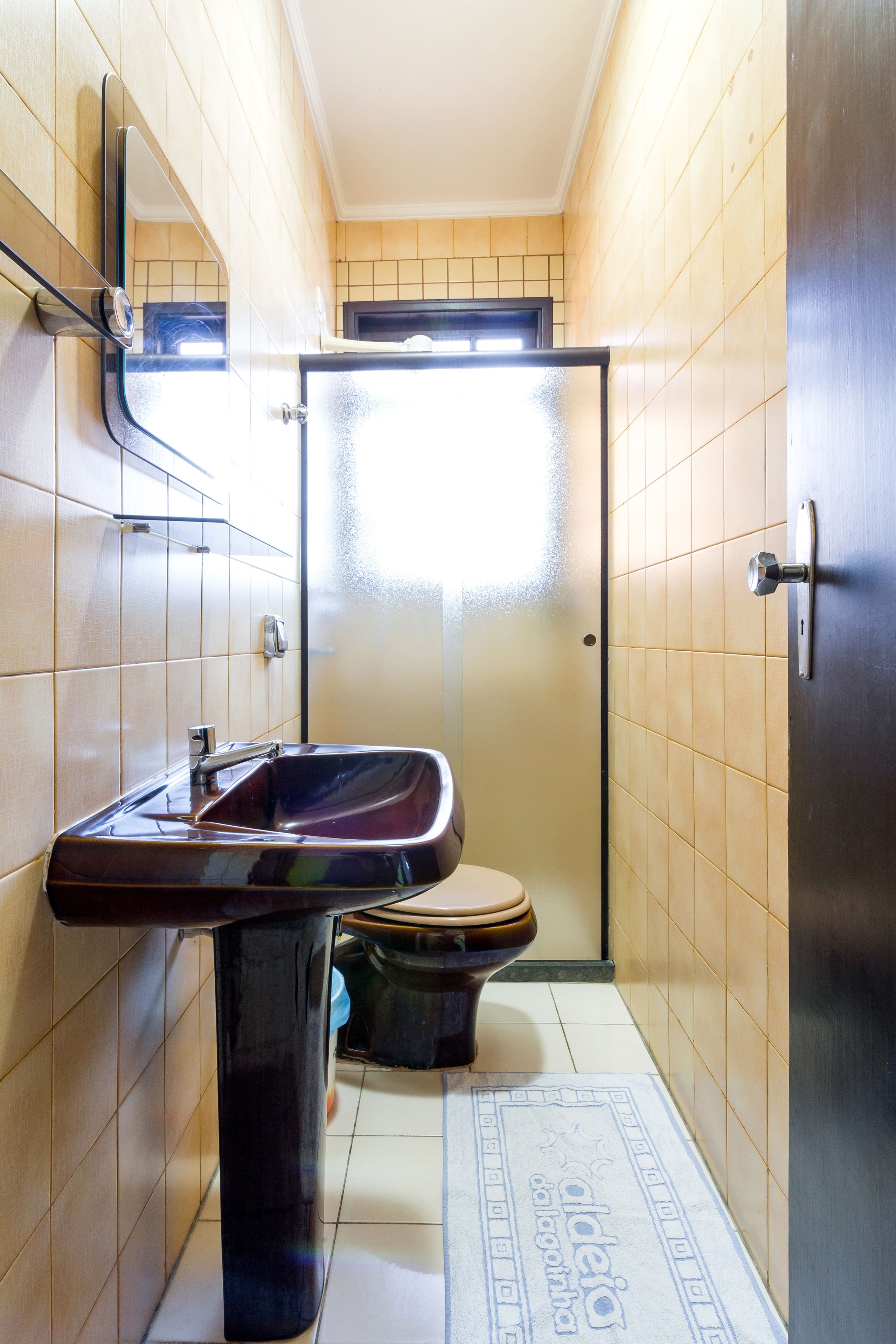 A compact bathroom with a sink, toilet, and a frosted glass shower door.