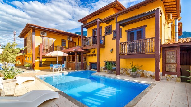 Un edificio de dos pisos con piscina, mobiliario exterior y vistas a la montaña.