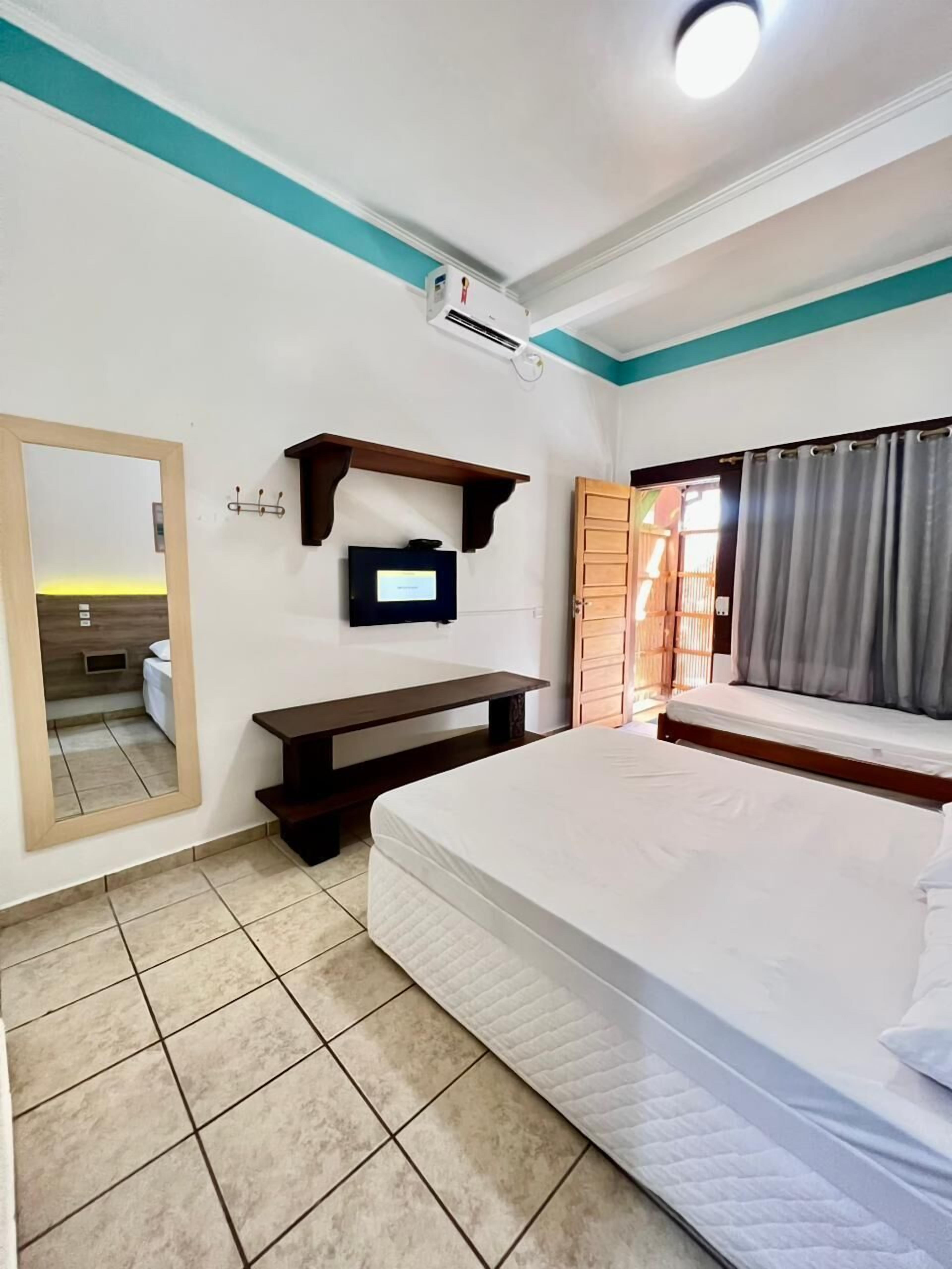 A hotel room with a bed, a TV, a mirror, a window with curtains, and a ceiling fan.