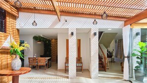 Un interior moderno con techo de madera, una zona de comedor con sillas y una mesa, y una planta grande en maceta.