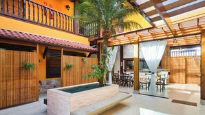Un espacio interior amplio con un banco de madera, una pequeña jardinera con una palmera y una zona de comedor con mesas y sillas.