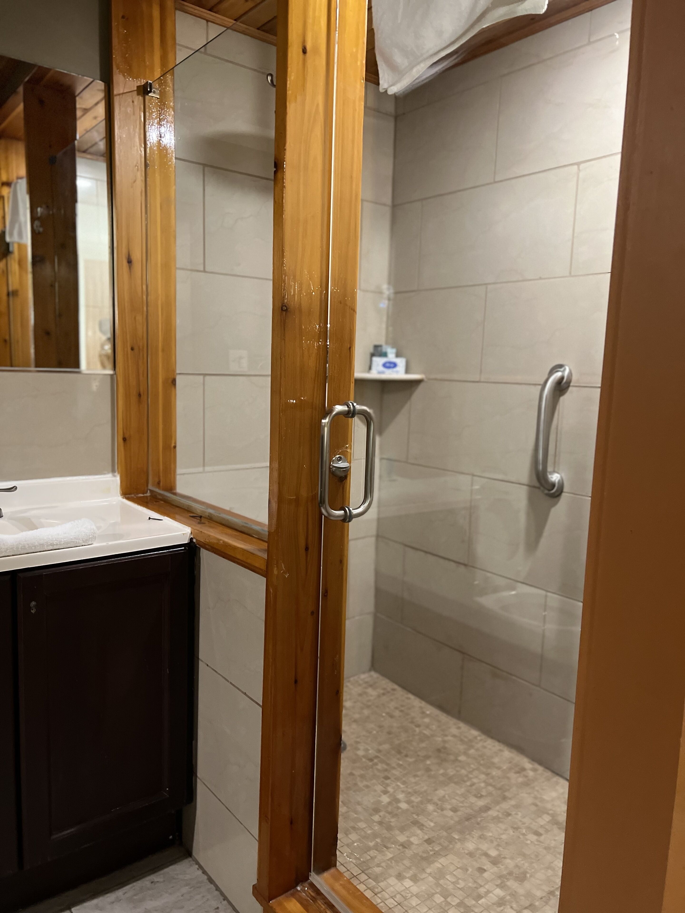 A shower area with a glass door, a wooden frame, and a tiled floor.