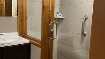 A shower area with a glass door, a wooden frame, and a tiled floor.