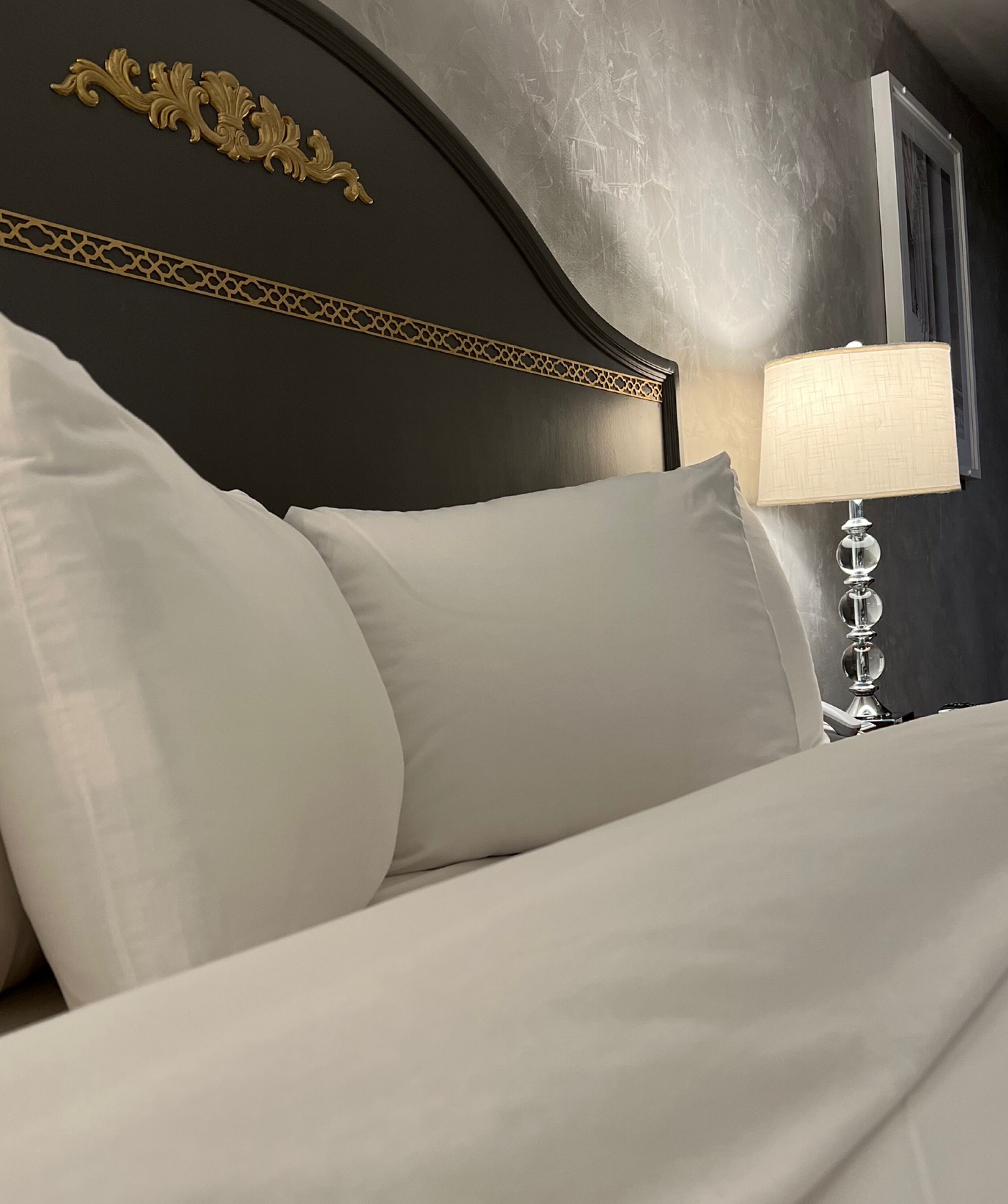 A bed with white bedding and a decorative headboard with gold accents.