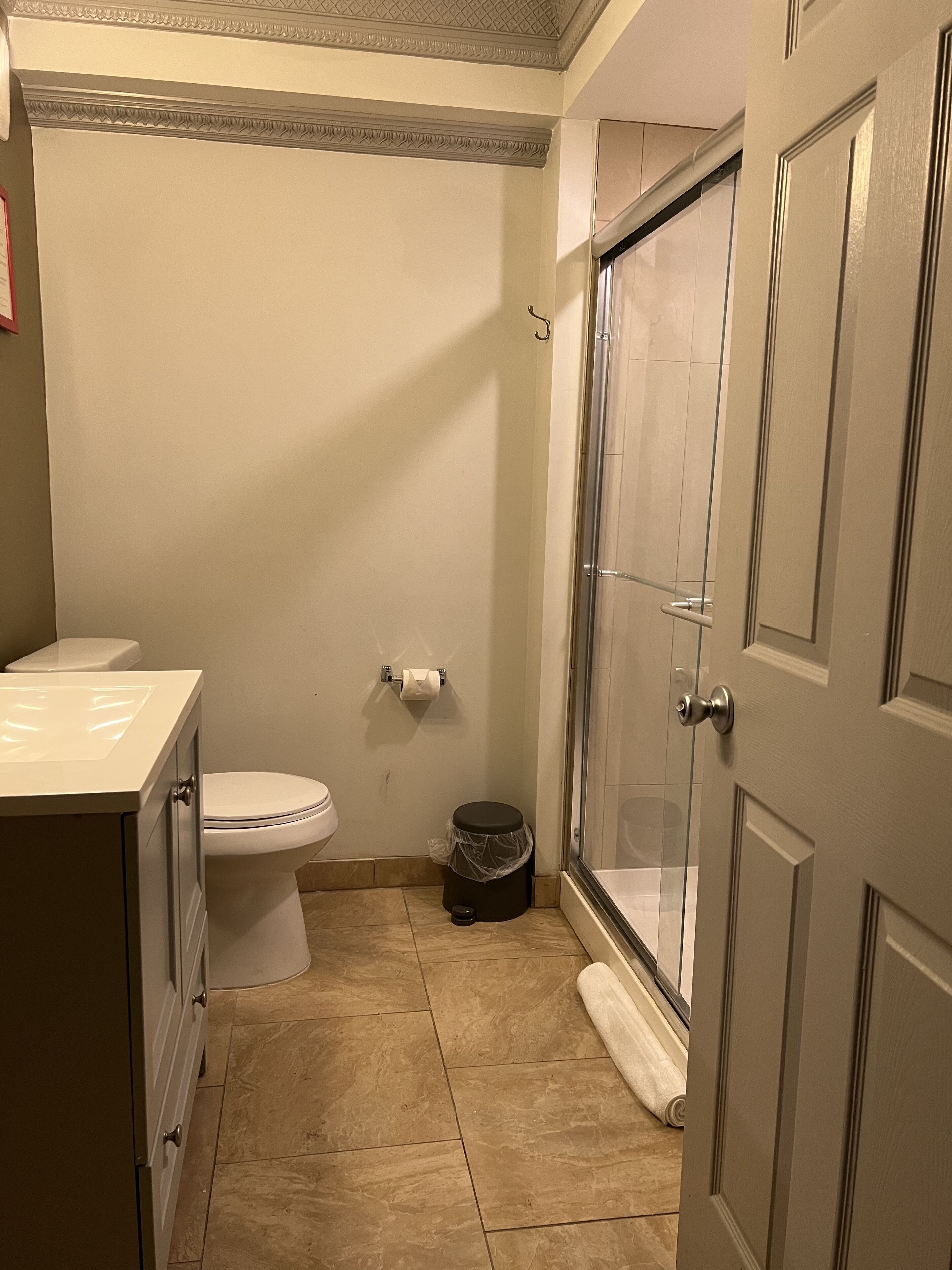 A bathroom with a toilet, sink, shower, and a trash can.