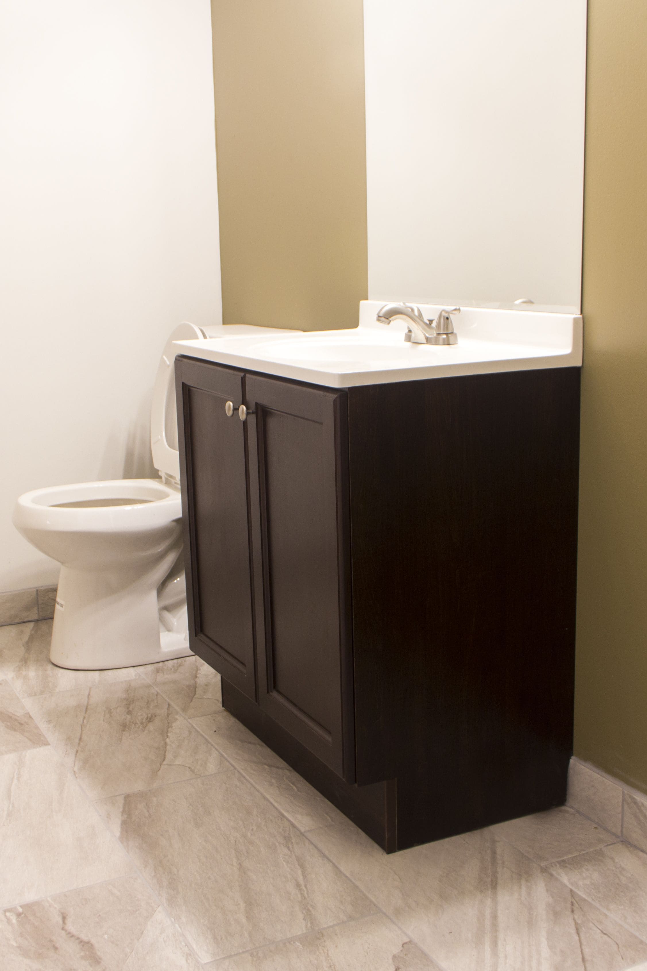 A bathroom with a white toilet, dark wooden cabinets, and a white sink.
