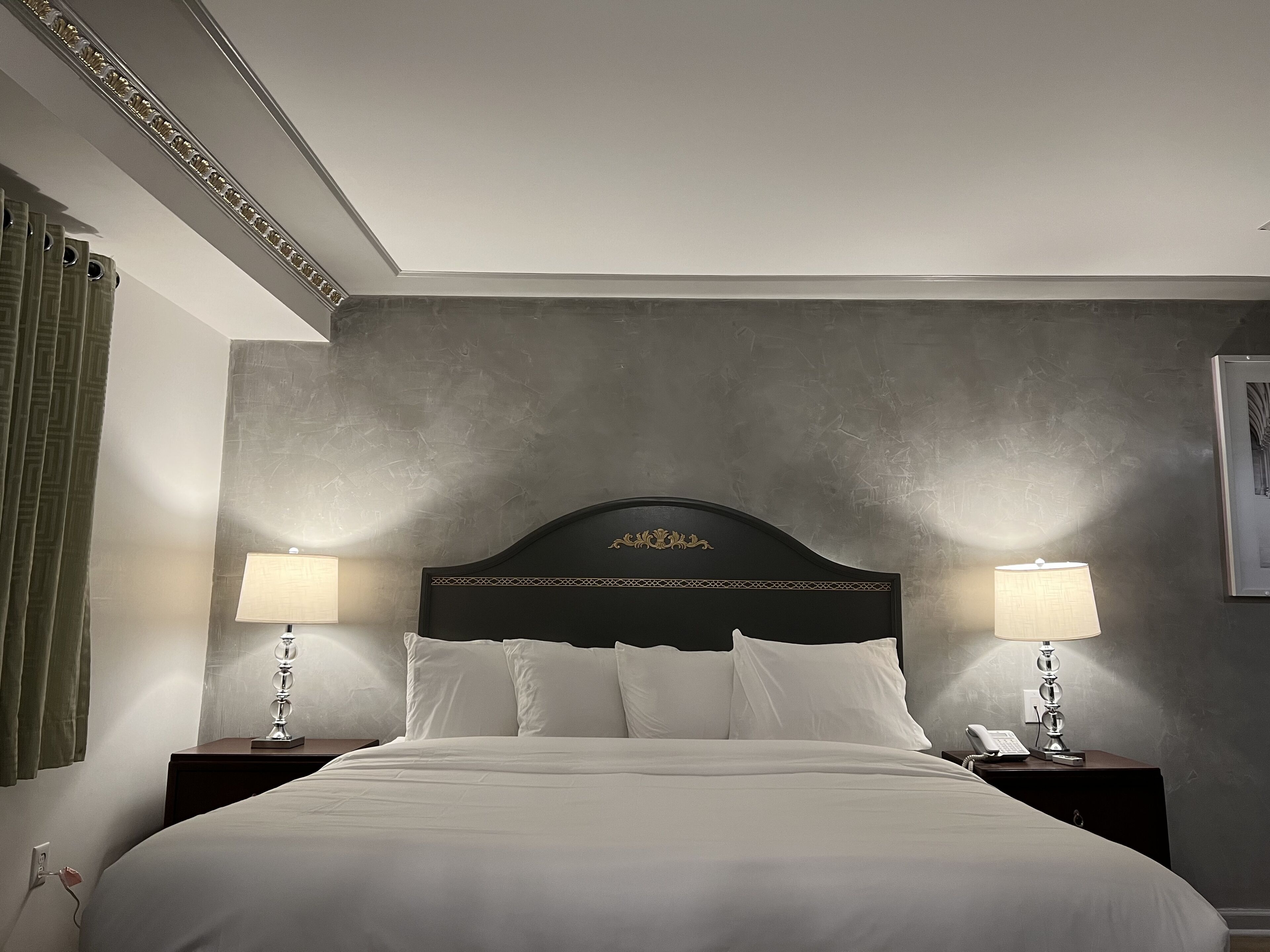 Una habitación de hotel con una cama grande, dos mesitas de noche con lámparas, un teléfono en la pared y un cuadro enmarcado.
