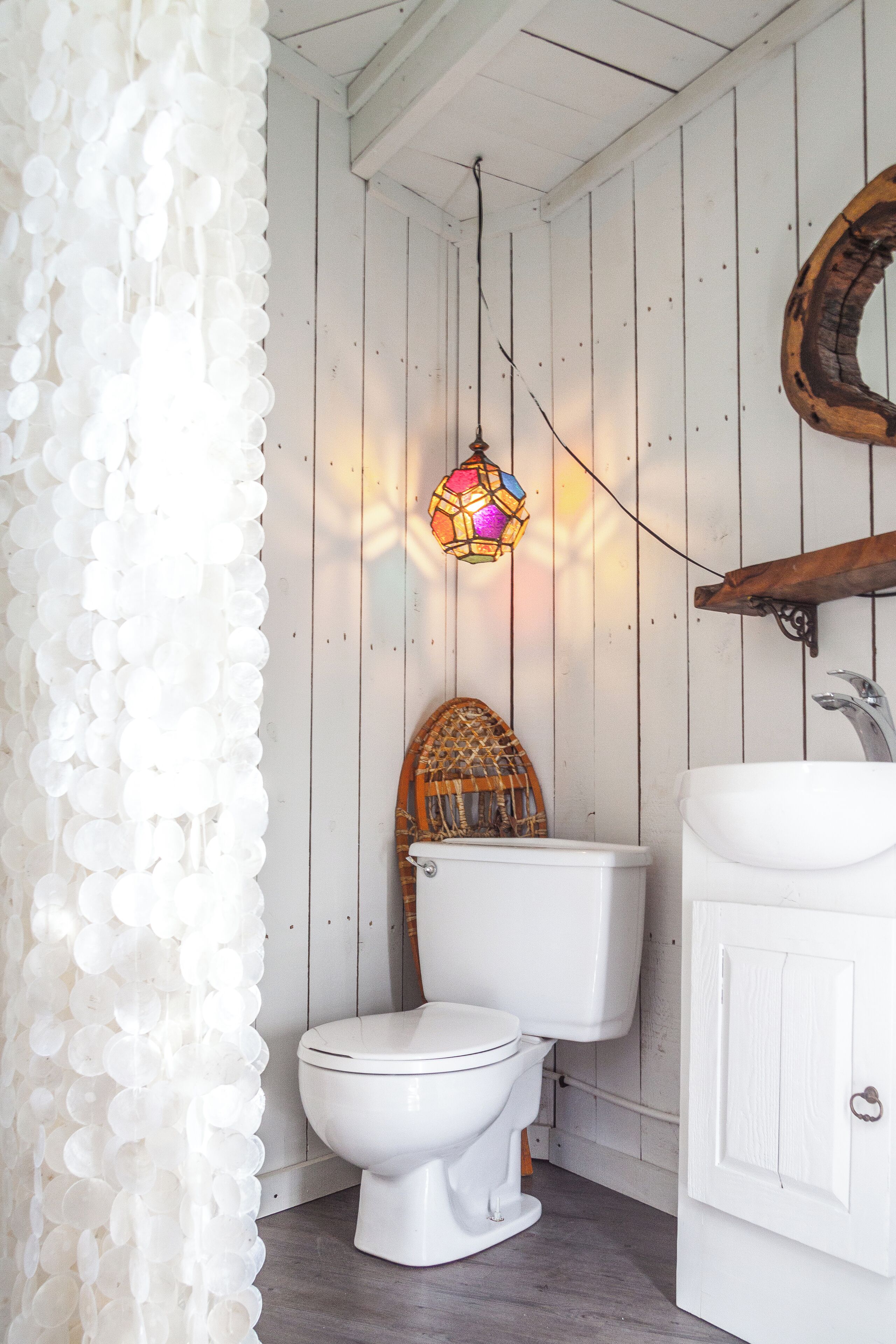 A bathroom with a white toilet, a wooden shelf, and a hanging light fixture.
