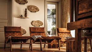 Une pièce comprenant une grande table en bois, deux chaises en bois, un tapis tissé et un mur orné d’assiettes décoratives et d’une petite statue.