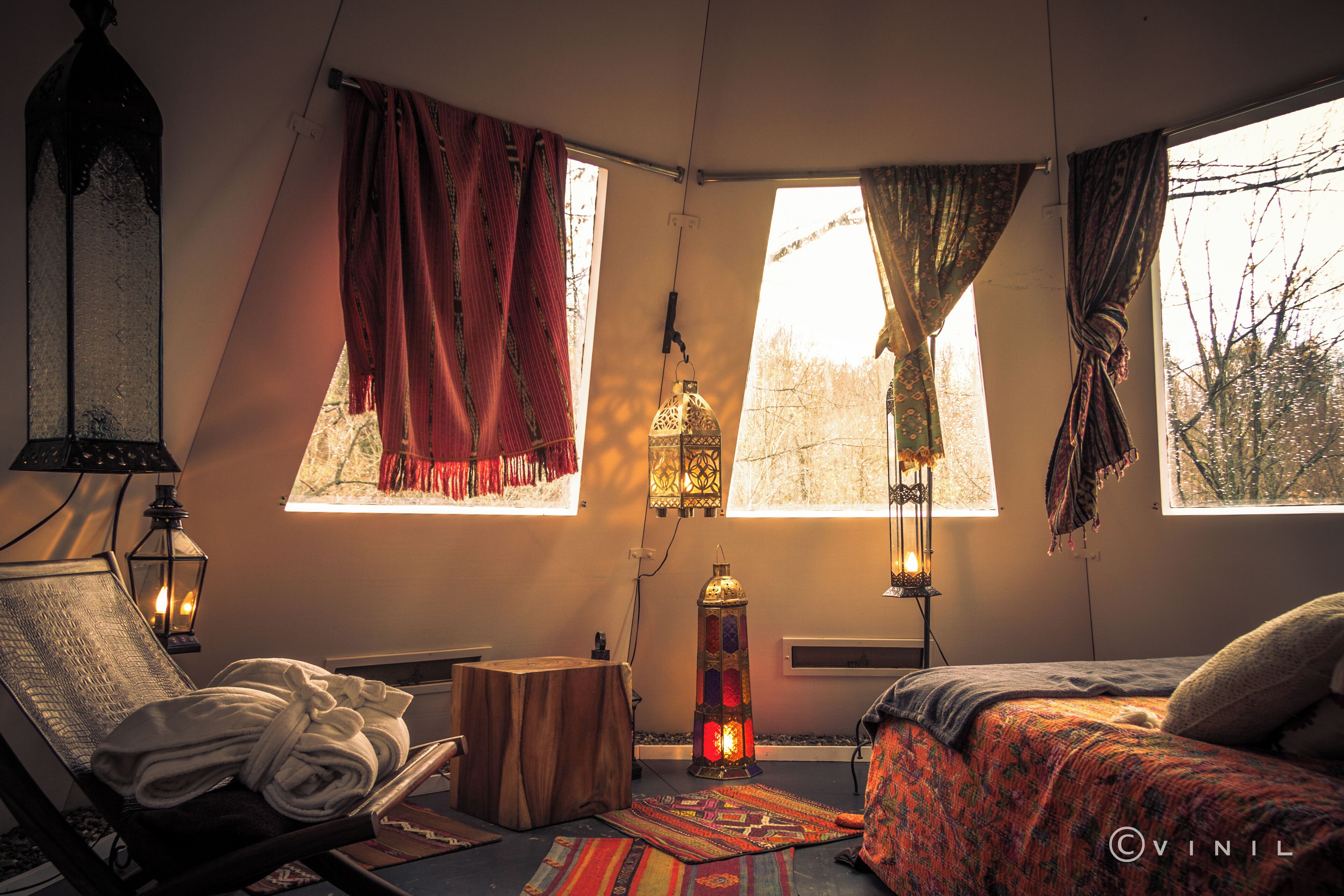 A cozy room with a bed, a chair with a towel, a small table, and two windows with curtains.