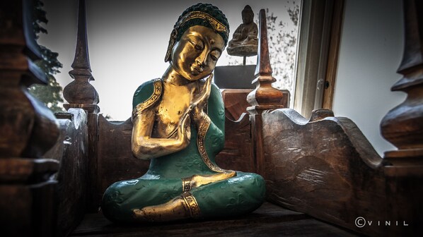 A Buddha statue in a meditative pose, seated on a wooden bench with intricate carvings. - Villa Nao (Roxton)