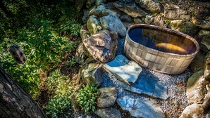 Un bain à remous en bois, entouré de rochers et de galets, avec un tronc d’arbre à proximité.