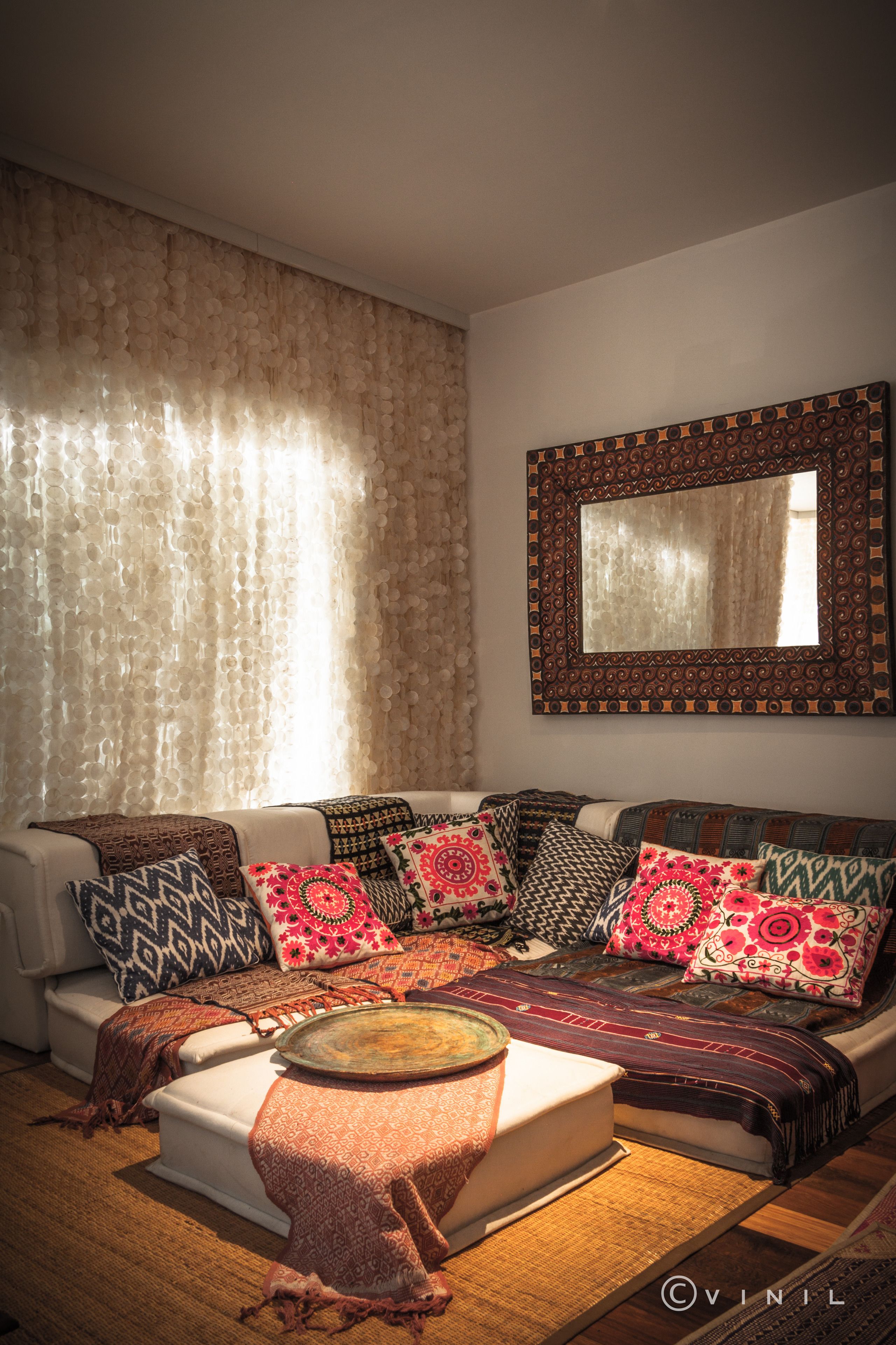 Una sala de estar con sofá, cojines estampados, una mesita de centro y un espejo decorativo.