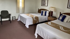 Et hotelværelse med to senge, en stol, et natbord, en lampe, et billede på væggen og et vindue med gardiner.