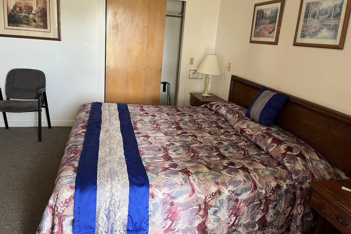 Ein Hotelzimmer mit einem großen Bett, einem Sessel, einer Holztür und zwei gerahmten Bildern an der Wand.