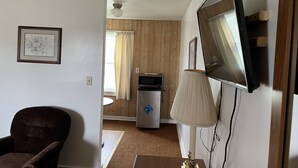 Et værelse med en brun lænestol, et tv ophængt på væggen, en lampe og et billede i ramme på væggen.