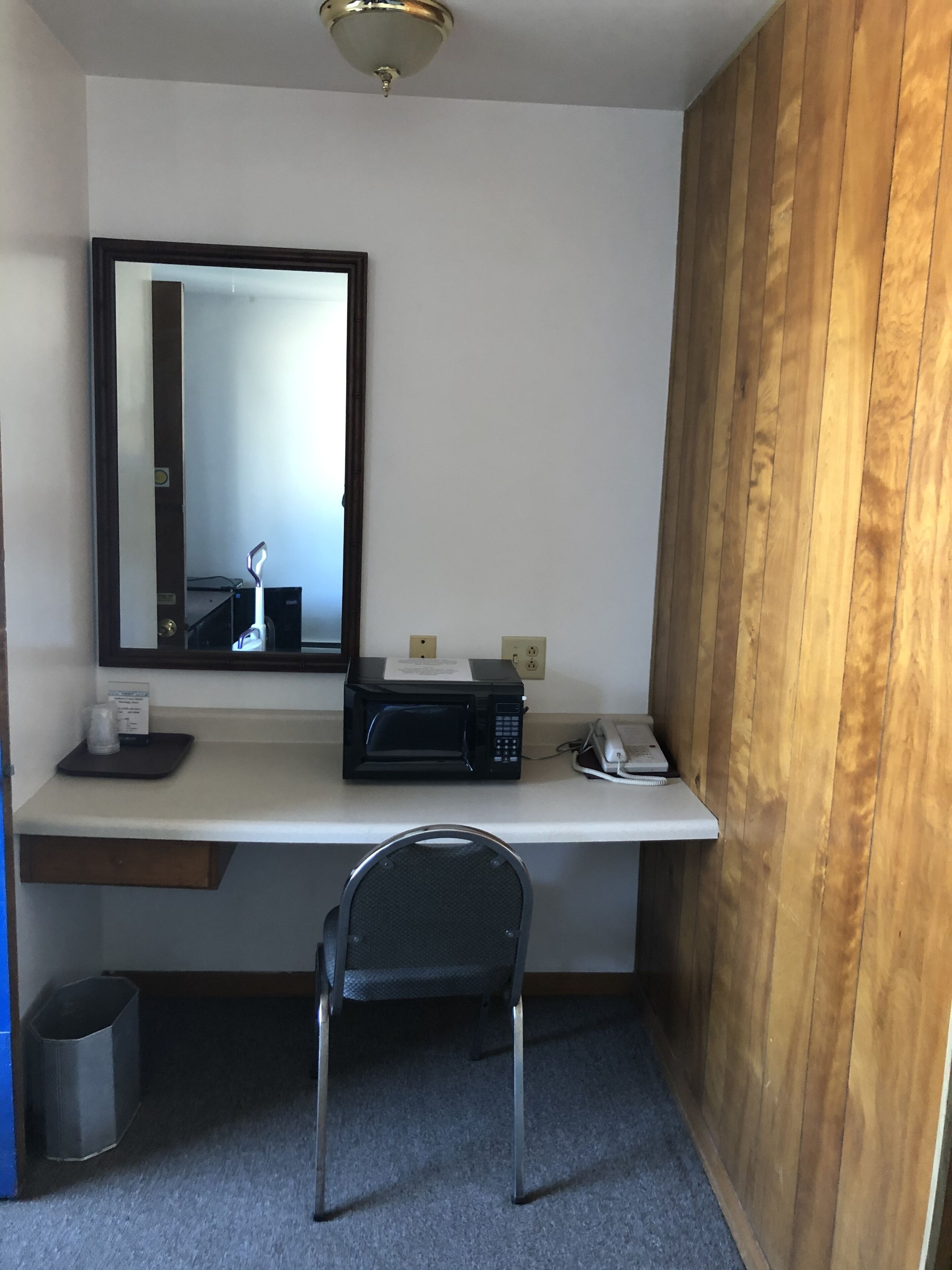 Habitación de hotel compacta con kitchenette, microondas, una mesita, una silla y un espejo.
