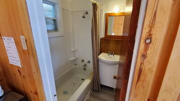 Une salle de bain aux murs lambrissés, équipée d’une baignoire, d’un lavabo et d’un miroir.