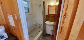 A wooden-paneled bathroom with a bathtub, a sink, and a mirror. - Motel Le Fleuron (Saint Donat)