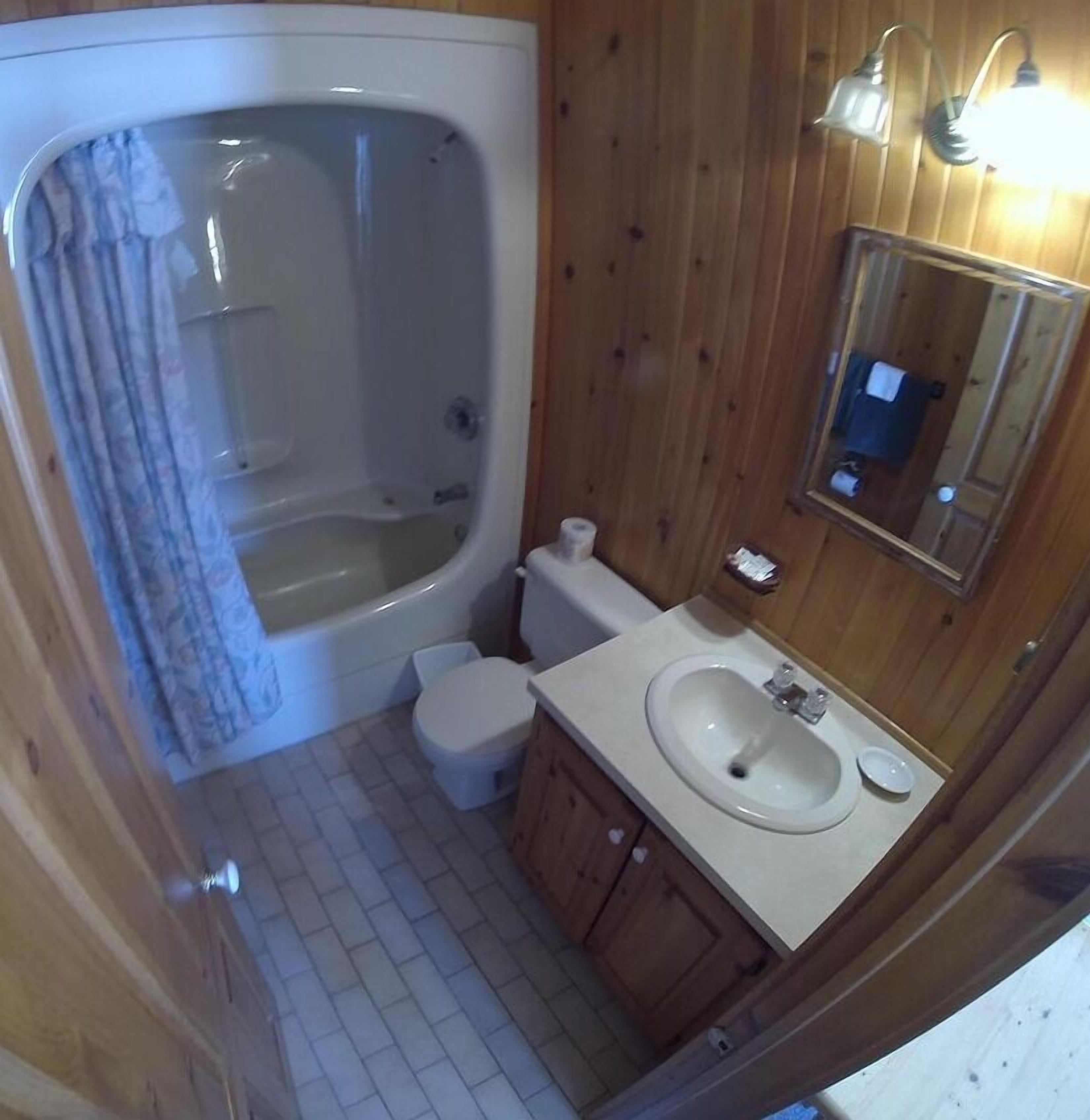 Un baño con bañera, inodoro, lavabo y armarios de madera.