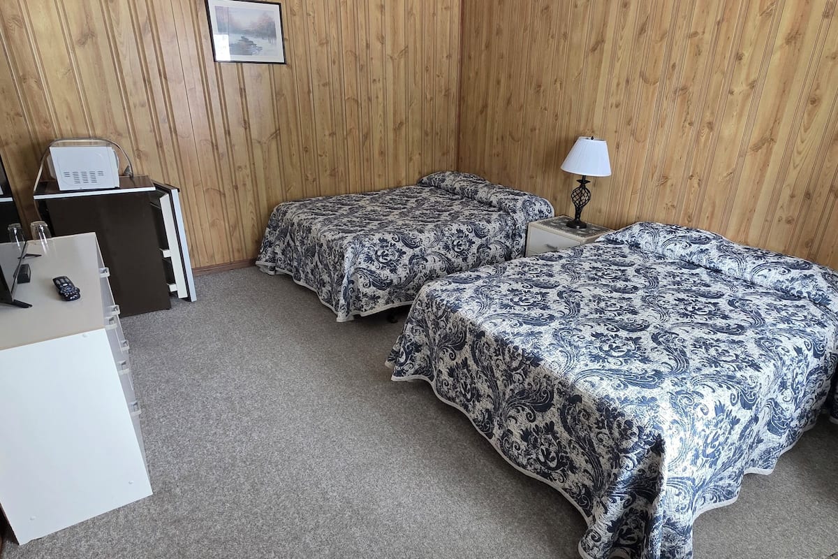 A hotel room with two beds, a desk with a computer, a lamp, and a small table with a picture frame.