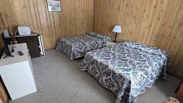 Habitación de hotel con dos camas, un escritorio con computadora, una lámpara y una mesita con un marco de fotos.