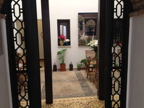 A courtyard with a tiled floor, a wooden chair, a table, and potted plants. - Hospedería Alma Andalusí (Córdoba)