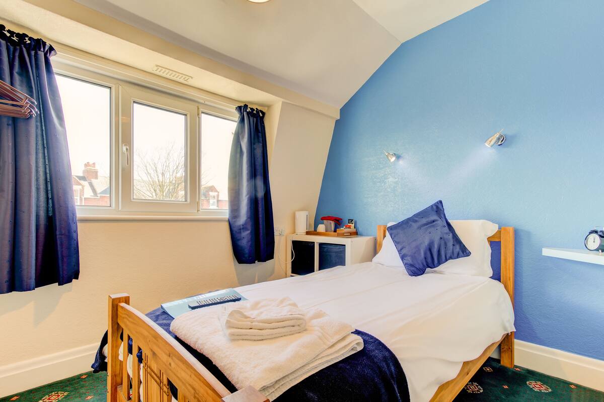 A bedroom with a bed, a bedside table, a window, and a wall clock.
