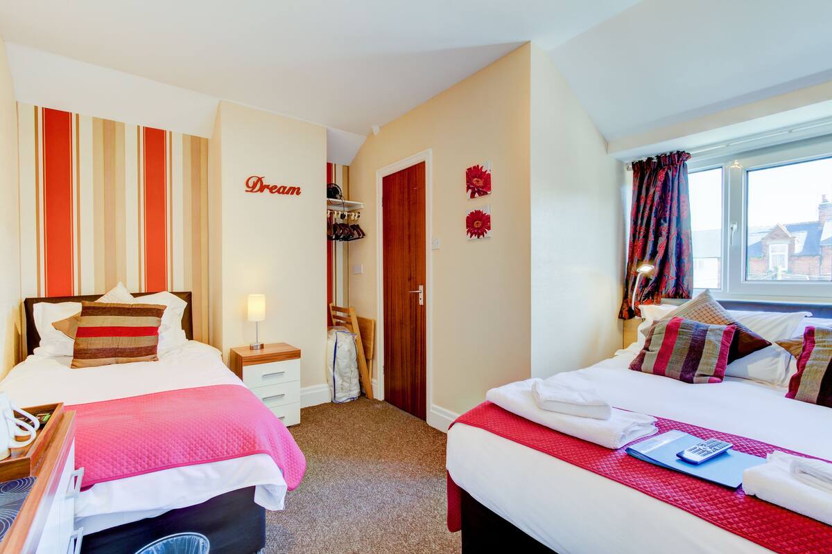 A hotel room with two beds, a wardrobe, a desk, and a window with curtains.