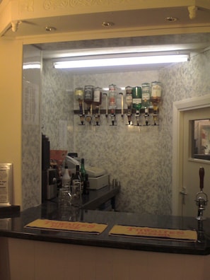 A bar area with a marble wall, a counter with a cash register, and a variety of liquor bottles. - Karden House (Llandudno)