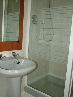 Un baño con un lavamanos blanco, un espejo y una cabina de ducha de vidrio.