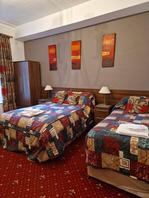 A hotel room with two beds, a wooden wardrobe, and three abstract paintings on the wall. - Karden House (Llandudno)