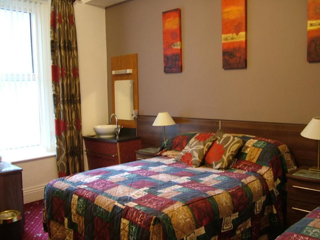 A hotel room with a bed, bedside lamps, a nightstand, a mirror, and artwork on the wall.