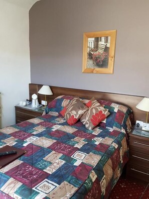 Una habitación de hotel con una cama grande, una mesita de noche, una lámpara y un cuadro en la pared.