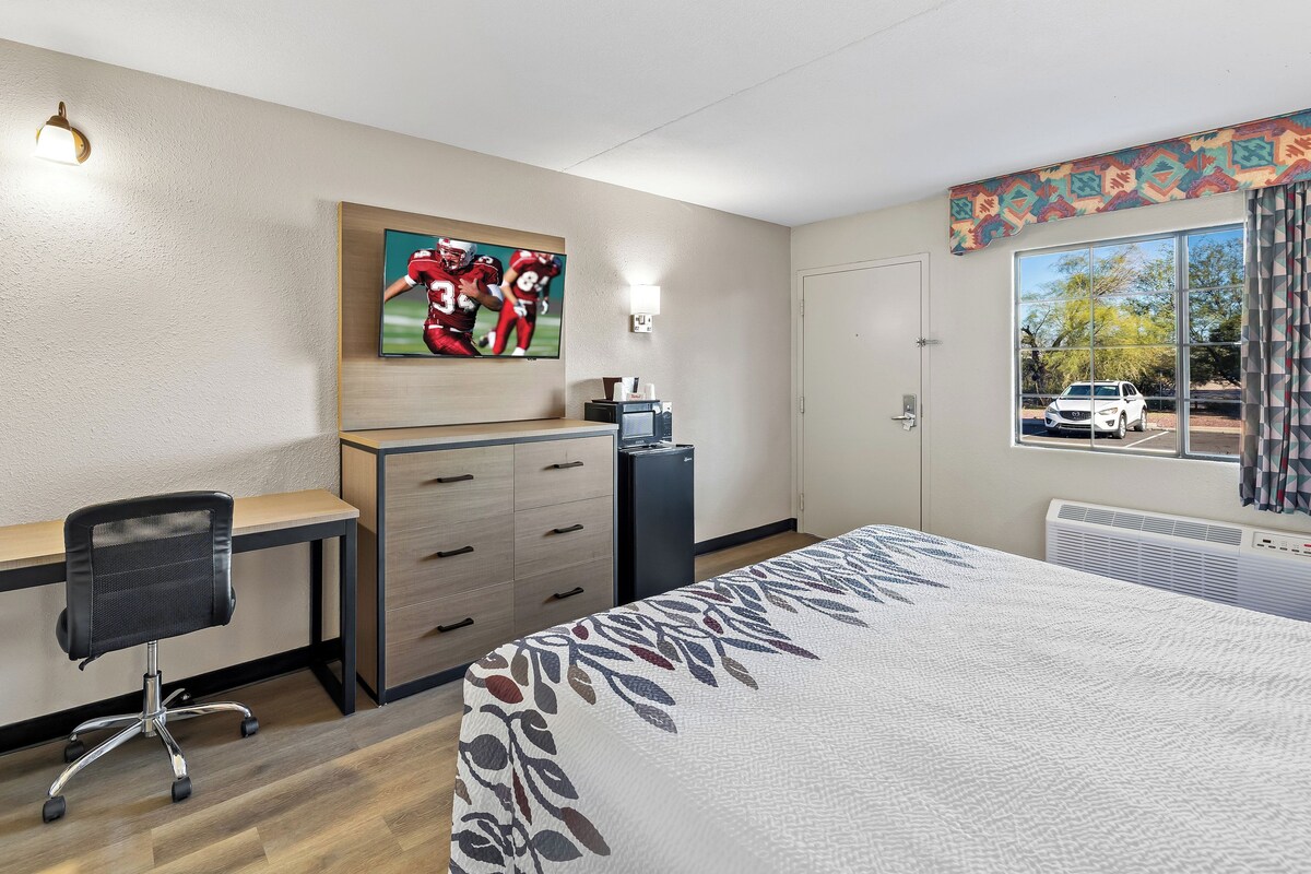 A hotel room with a bed, desk, chair, and a television mounted on the wall.