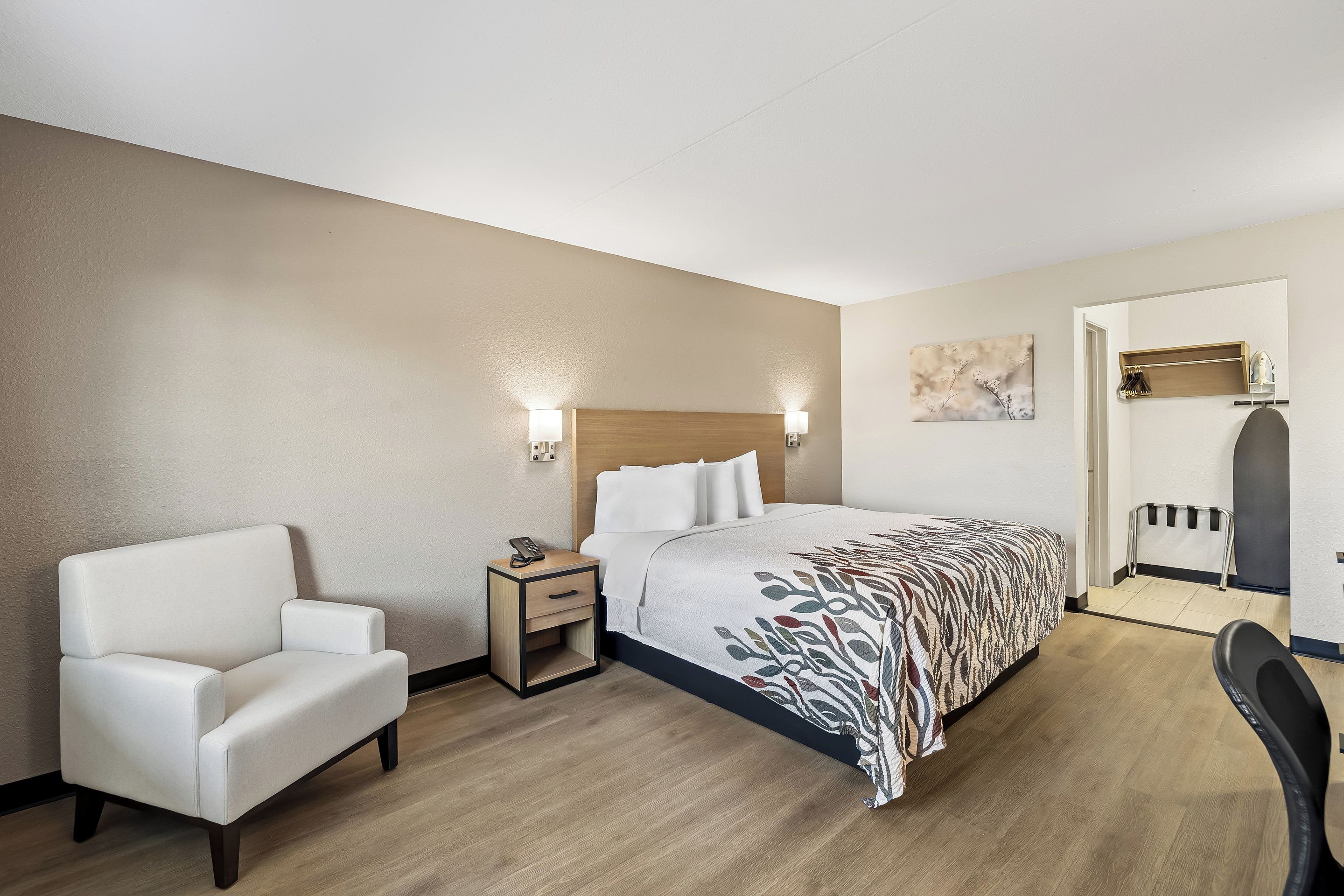 Una habitación de hotel con cama, una silla, una mesita de noche y un escritorio.
