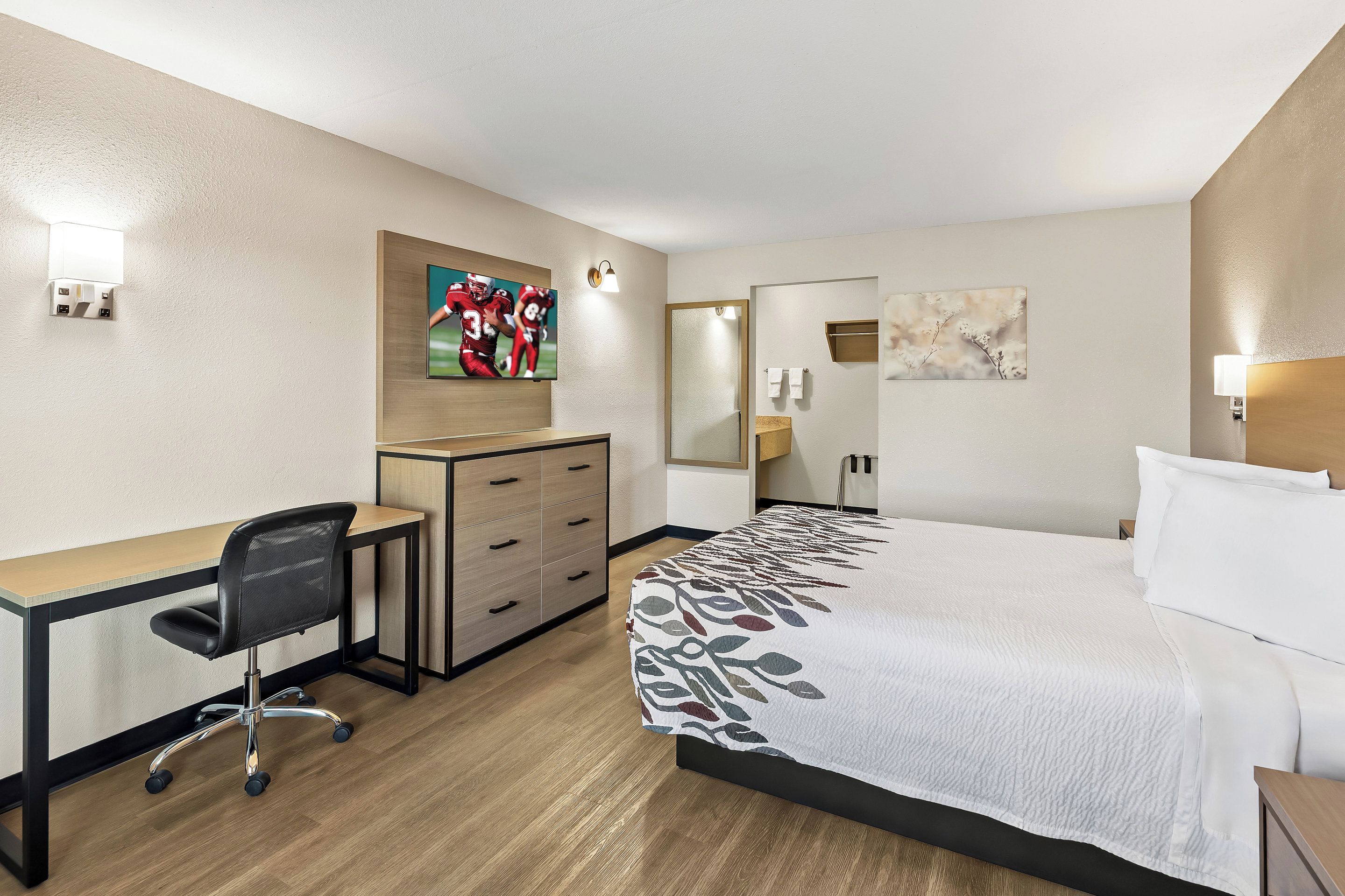 A hotel room with a bed, a desk, a chair, a TV, and a bathroom.