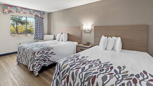 A hotel room with two beds, a window with a view, a nightstand, and a wall-mounted light fixture. - Red Roof Inn Tucson – Vail (Tucson)