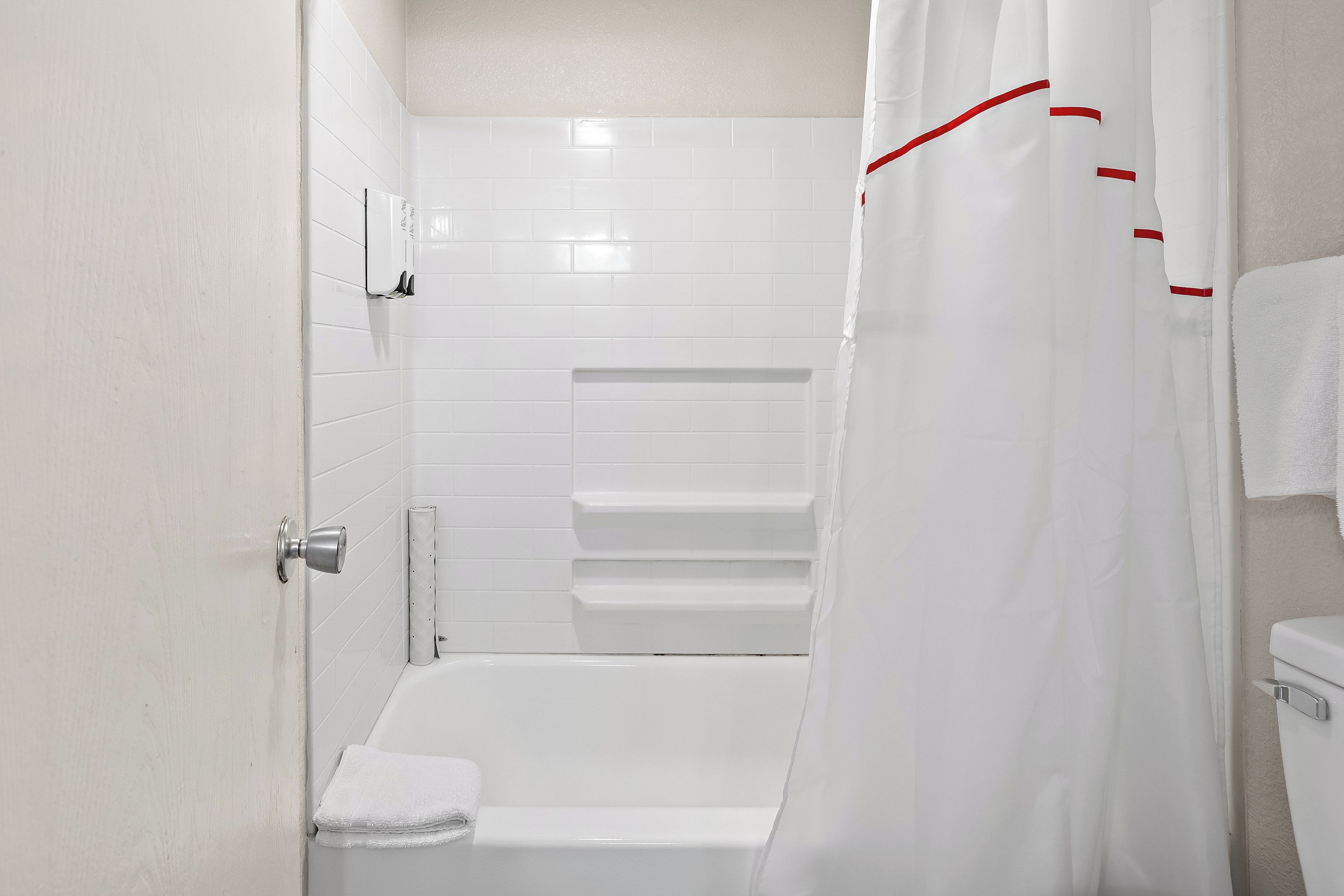 A bathroom with white tiles, a bathtub, a shower curtain, and a towel rack.