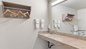 A bathroom with a granite countertop sink, a mirror, and wooden hangers on a wall-mounted rack.