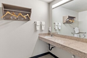 A bathroom with a granite countertop sink, a mirror, and wooden hangers on a wall-mounted rack.