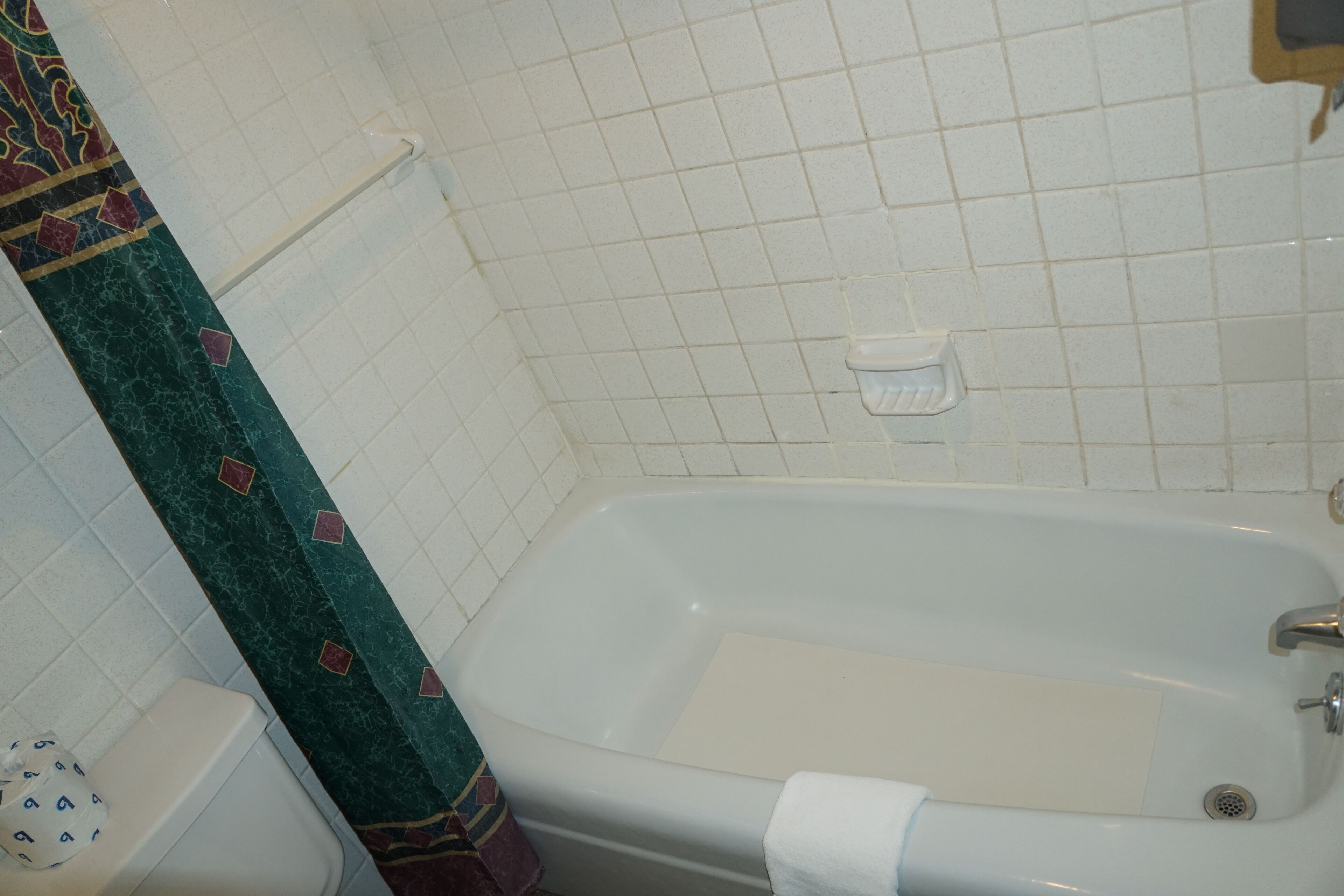 Un baño con una bañera blanca, un inodoro y una cortina de ducha con un diseño geométrico.