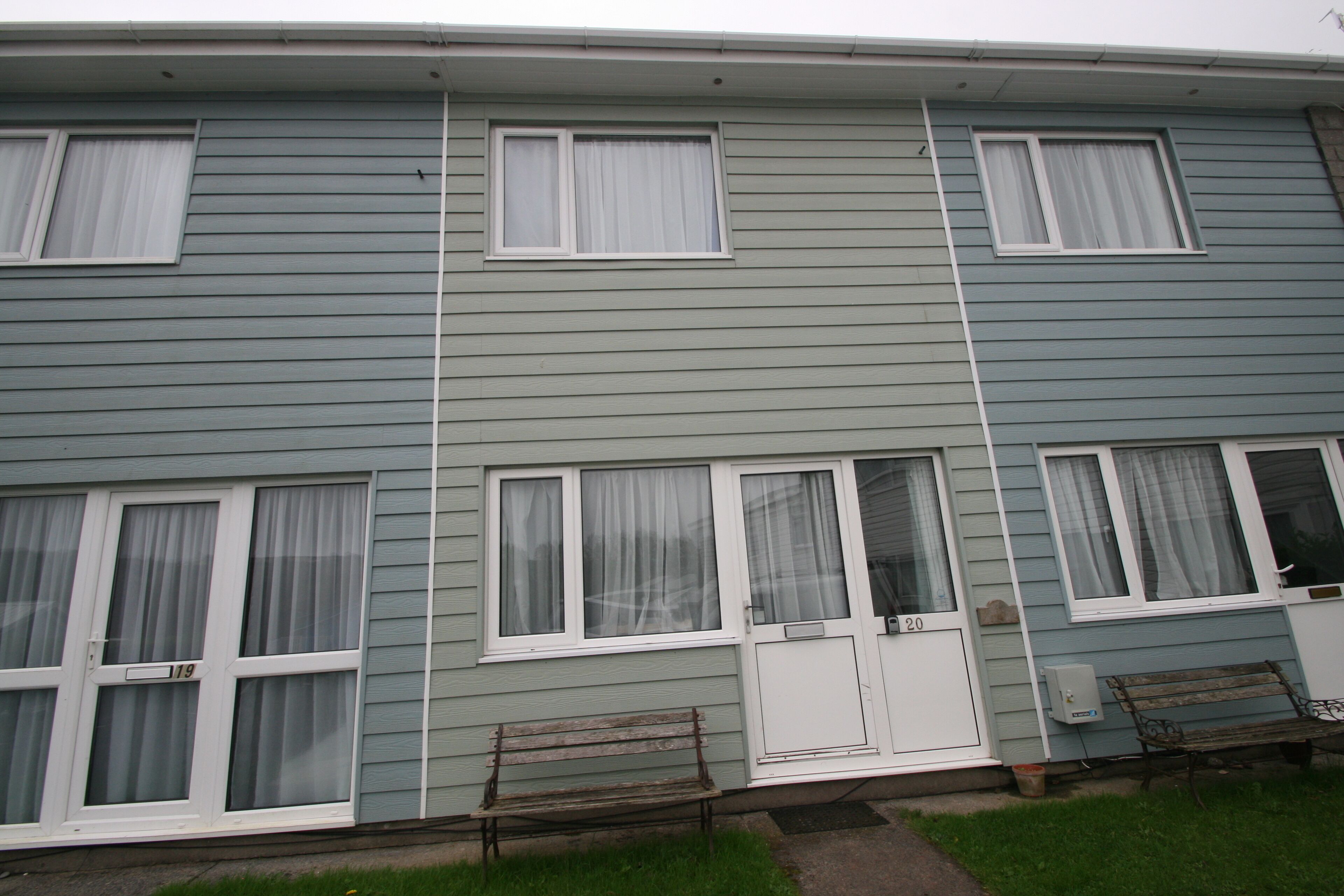 A two-story building with multiple windows, a front door, and two benches outside.