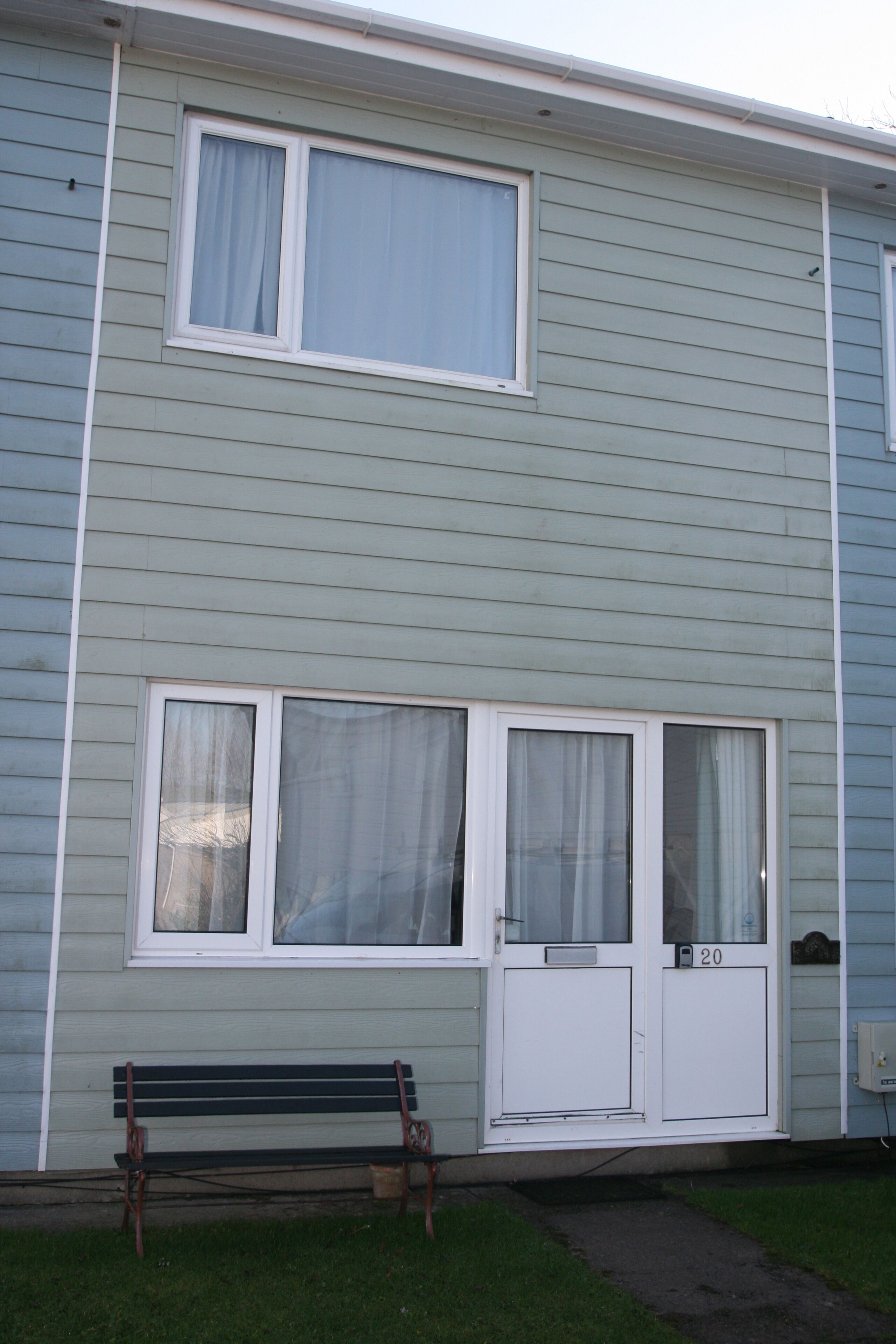 A two-story building with a front door, two windows, and a bench outside.