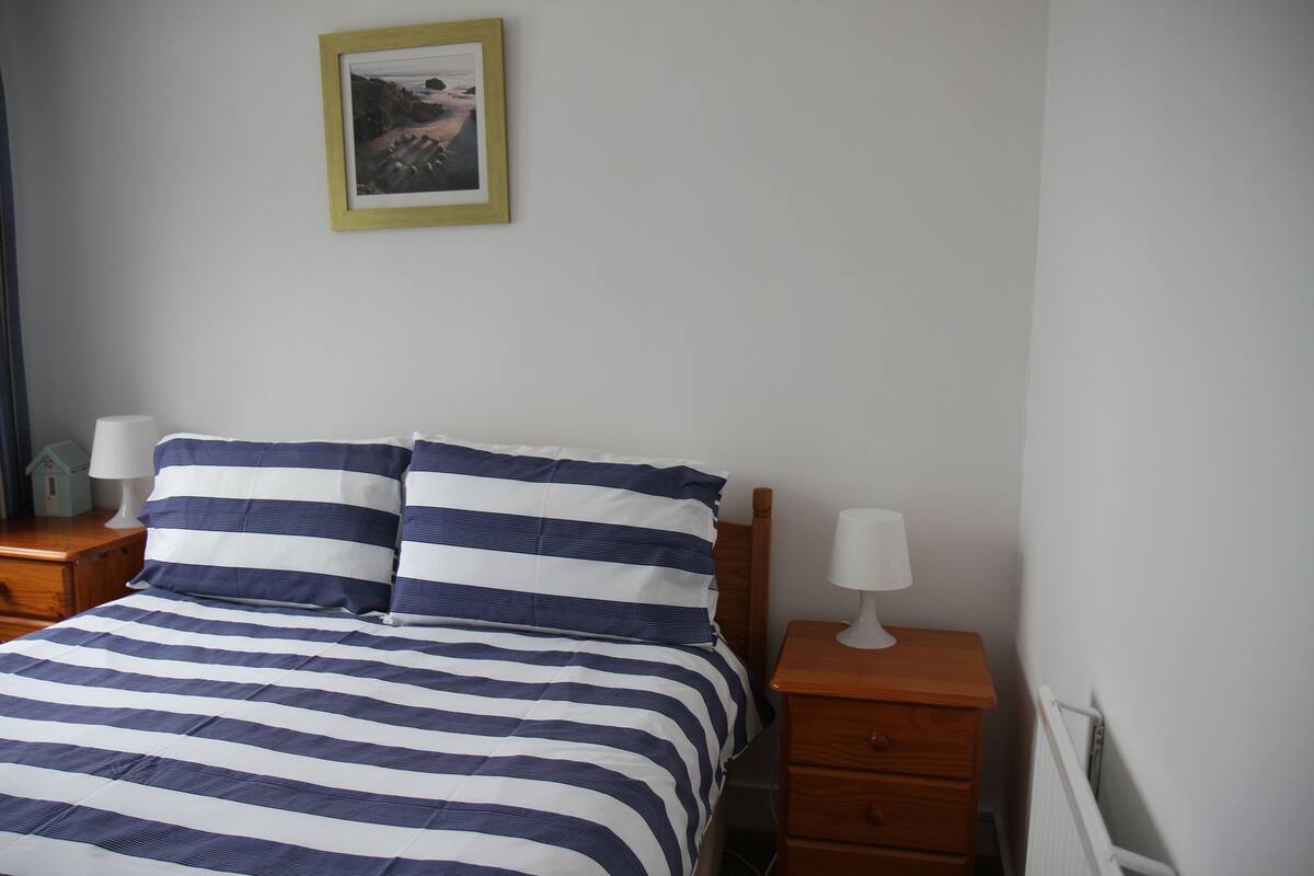 A neatly made bed with striped bedding, a bedside table with a lamp, and a framed picture on the wall.